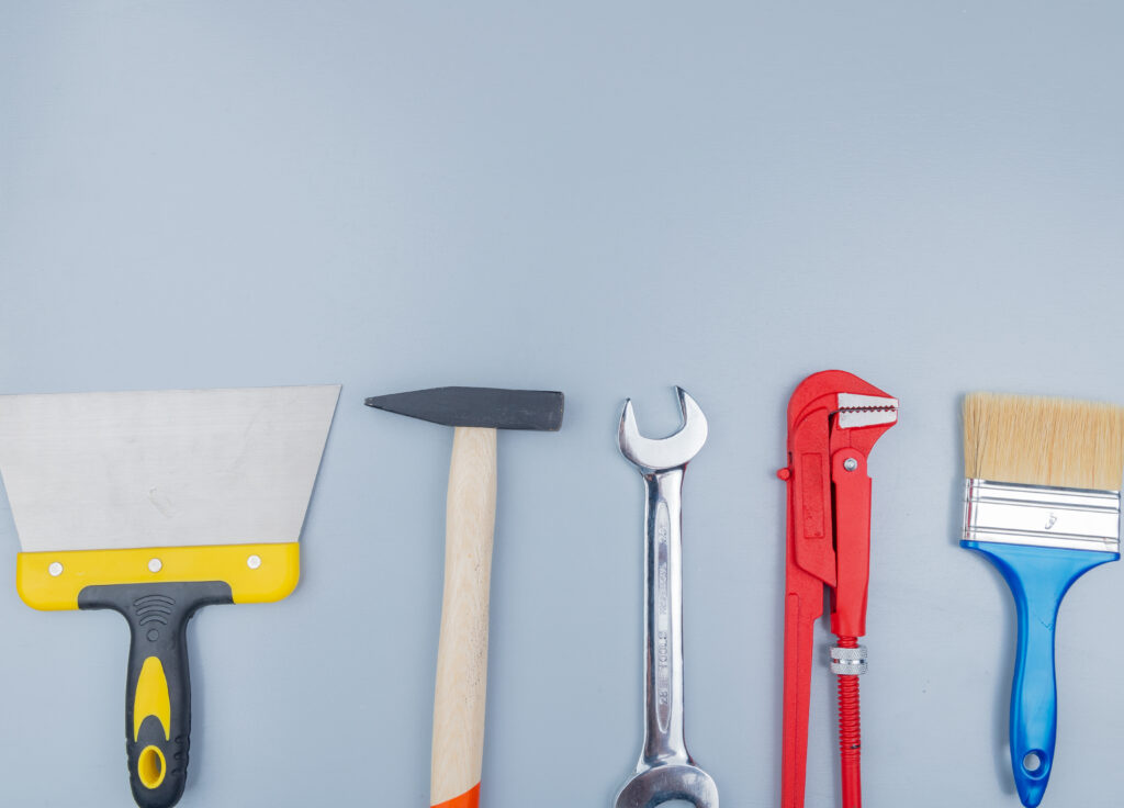 top view of construction tools as brick hammer pipe wrench putty knife paint brush and open-end wrench on gray background with copy space